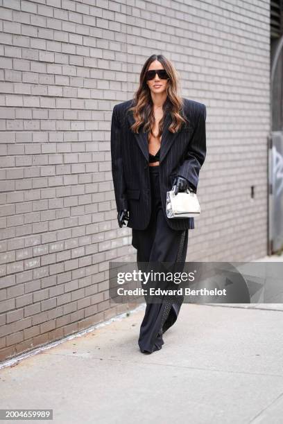 Tamara Kalinic wears sunglasses, a black striped oversized blazer jacket, black bras , a silver bag, black leather gloves, black flared pants ,...