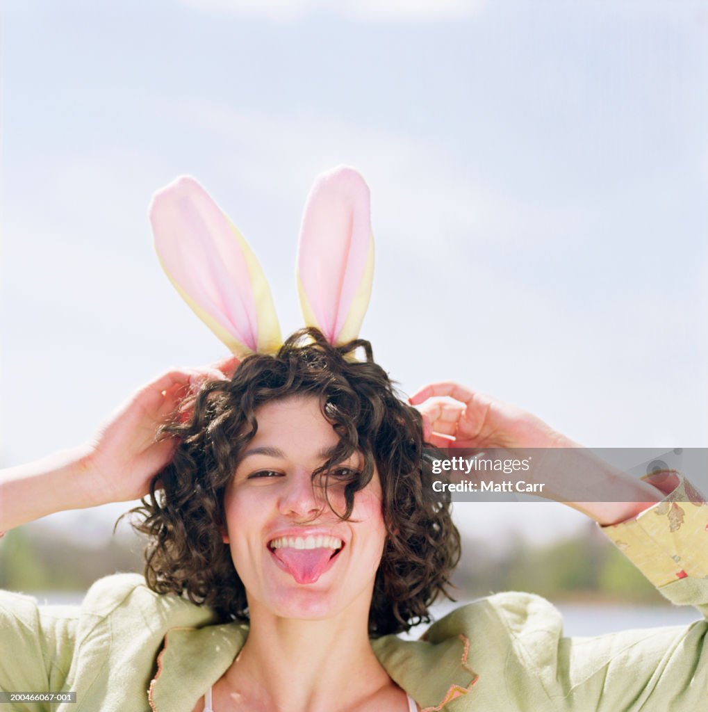 Young woman wearing pink rabbit ears, sticking tongue out