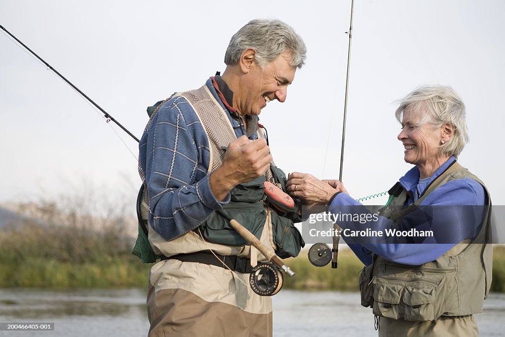 Senior man and woman with fly-fishing gear beside river, side view