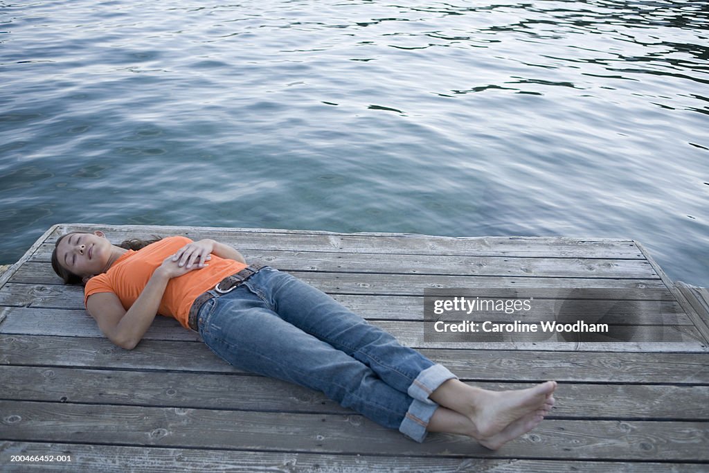 Young woman lying on dock, legs crossed at ankle, elevated view