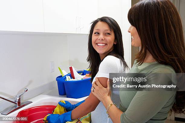 girl (13-15) at sink in laundry room, smiling at mother - washing tub stockfoto's en -beelden