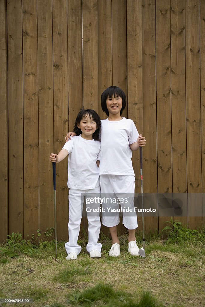 Brother and sister (8-10) with golf clubs, smiling, portrait