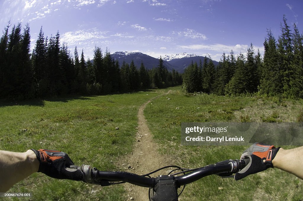 Man riding mountain bike on dirt footpath, mountains in background