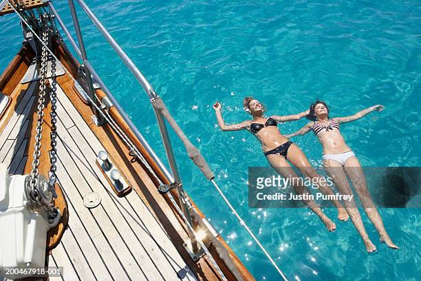 two young women floating in sea by sailboat, elevated view - navegación en yate fotografías e imágenes de stock