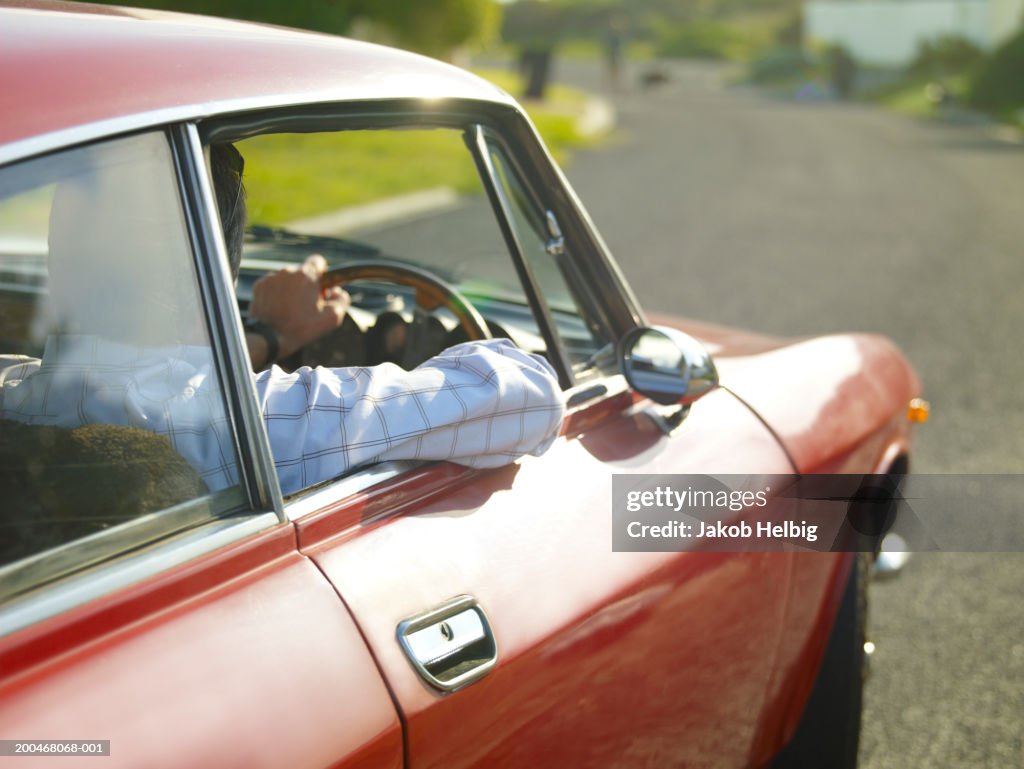 Mature man driving car, resting arm on door, rear view