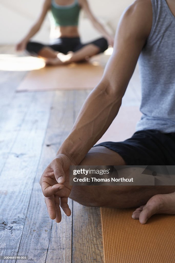 Two people in yoga class, low section (focus on man meditating)