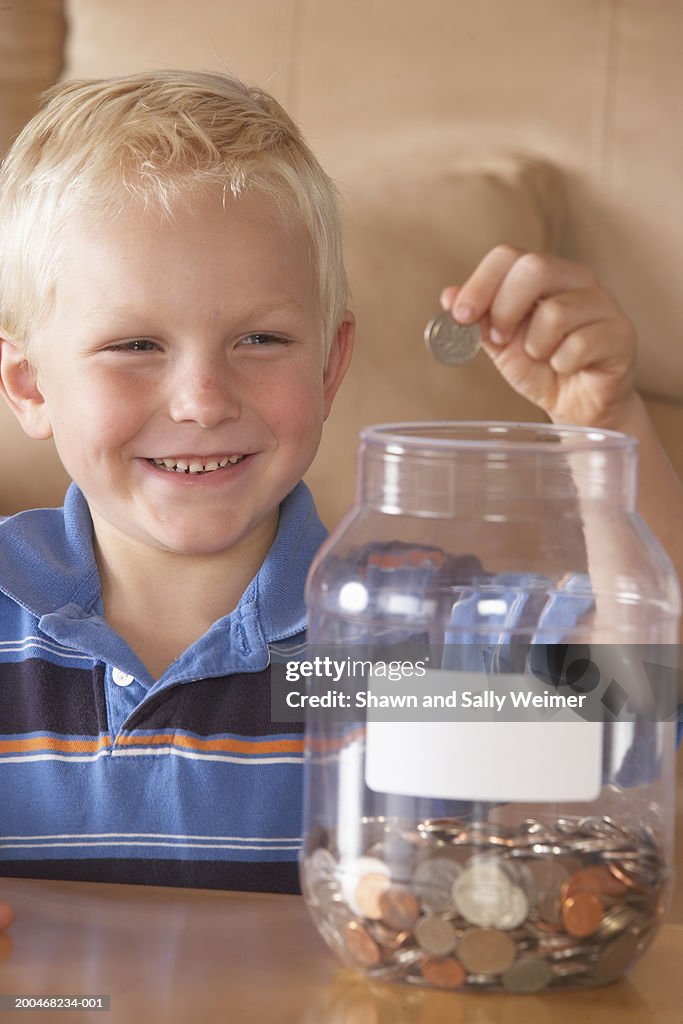 Boy (4-6) putting US coins into donation jar, smiling