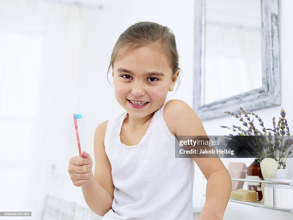 Girl (5-7) holding toothbrush, smiling, portrait