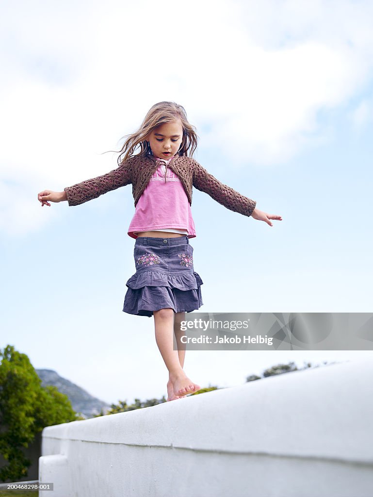 Girl (5-7) balancing on wall, outdoors, low angle view