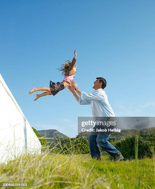 girl (5-7) jumping off wall into father's arms, outdoors, low angle - auffangen stock-fotos und bilder