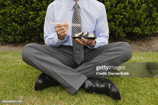 business man sitting on grass, eating sushi, low section, close-up - skjorta och slips bildbanksfoton och bilder