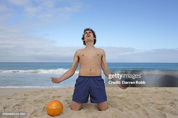 young man kneeling on beach, clenching fists, cheering, close-up - swimming trunks stock pictures, royalty-free photos & images