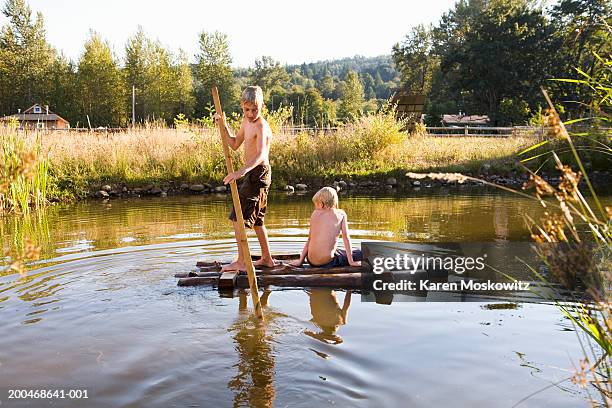 two boys (7-9) floating on wooden raft in pond - floß stock-fotos und bilder