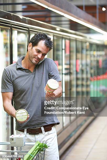 mature man using cell phone while selecting ice cream in supermarket - man eye cream stock pictures, royalty-free photos & images