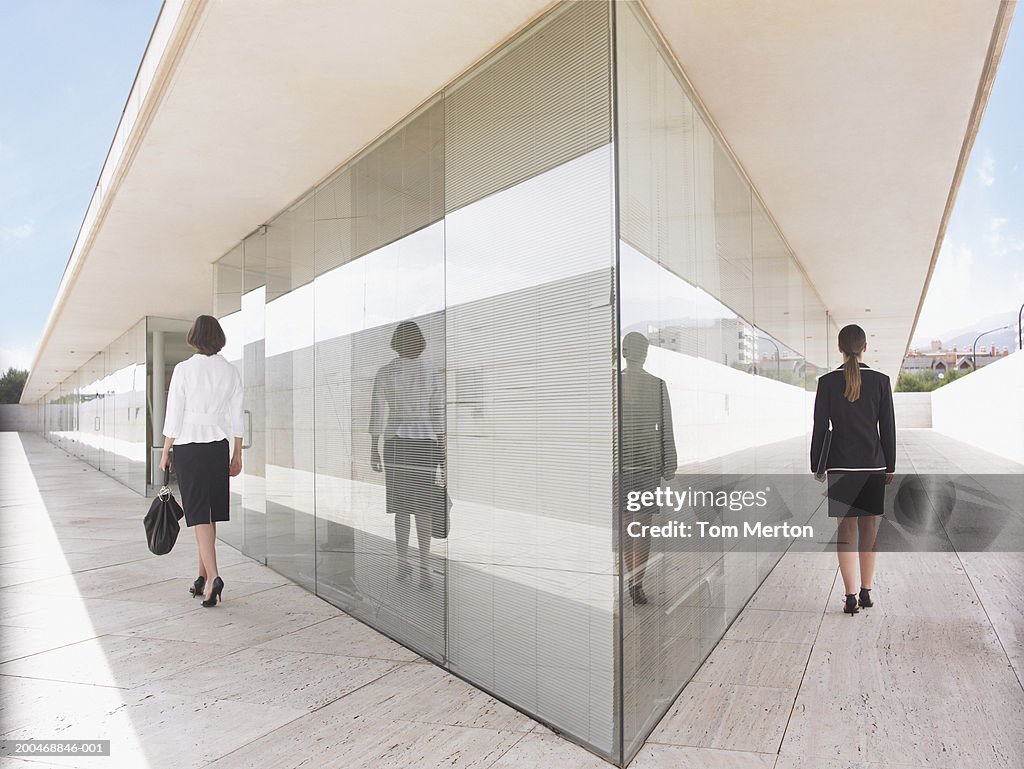 Two businesswomen walking either side of building, rear view