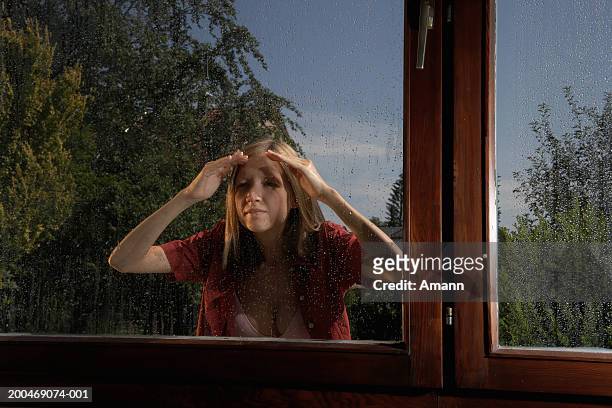 young woman looking through window, standing outside in rain - peep window stock-fotos und bilder