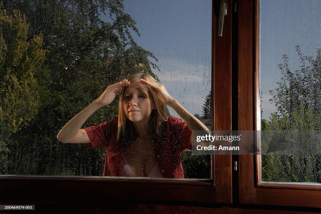 Young woman looking through window, standing outside in rain