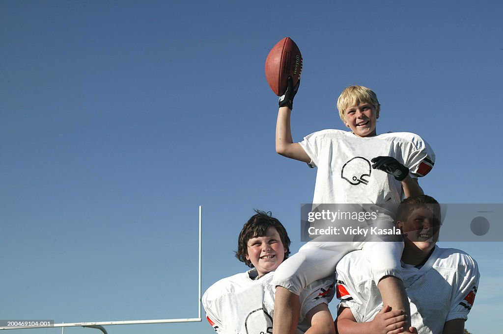 Two football players (10-12) carrying teammate on shoulders, smiling