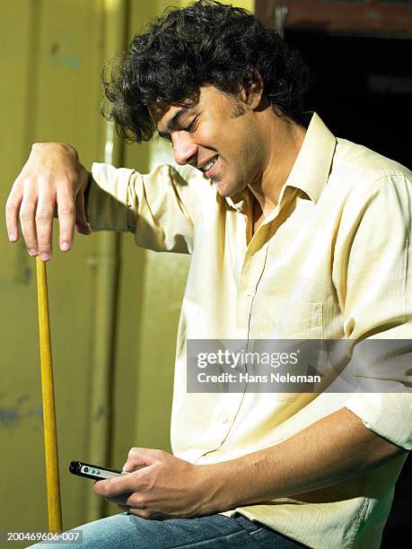 young man with pool cue looking at mobile phone - cue stock pictures, royalty-free photos & images