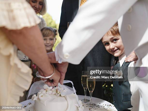 "Bride and groom cutting wedding cake, boy (6-7) smiling, portrait"