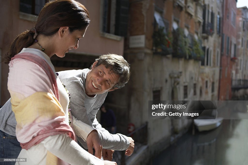 Couple relaxing beside canal, smiling at each other