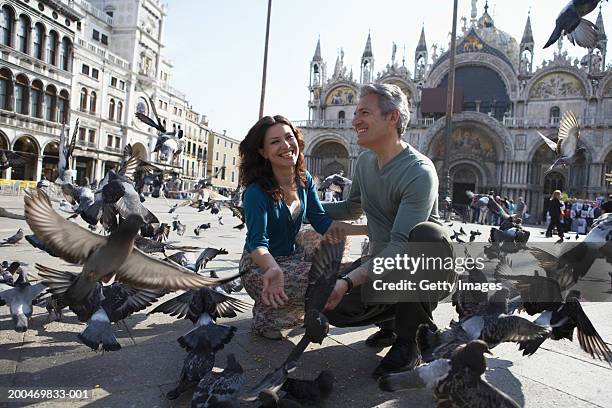 italy, venice, piazza san marco, couple crouching amongst pigeons - saint mark stock pictures, royalty-free photos & images
