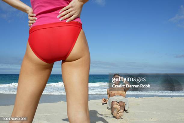 young man lying on beach, looking up at woman in foreground - long legs women stock-fotos und bilder