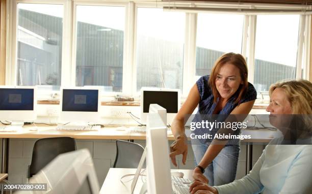 woman helping mature woman in computing class, pointing at screen - computer training stock pictures, royalty-free photos & images