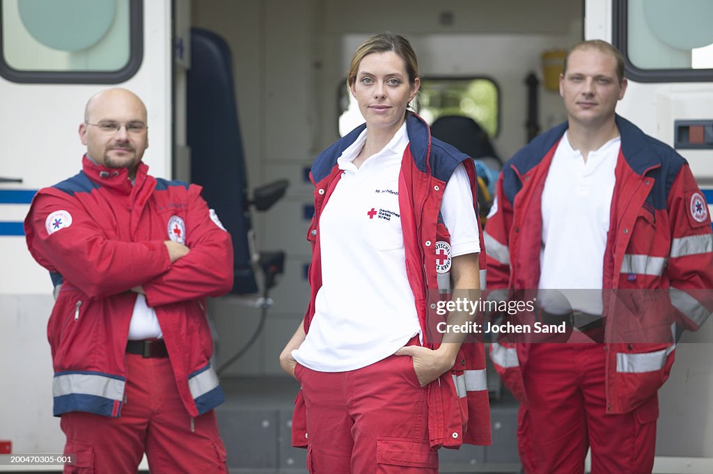 "Three paramedics standing beside ambulance, portrait"