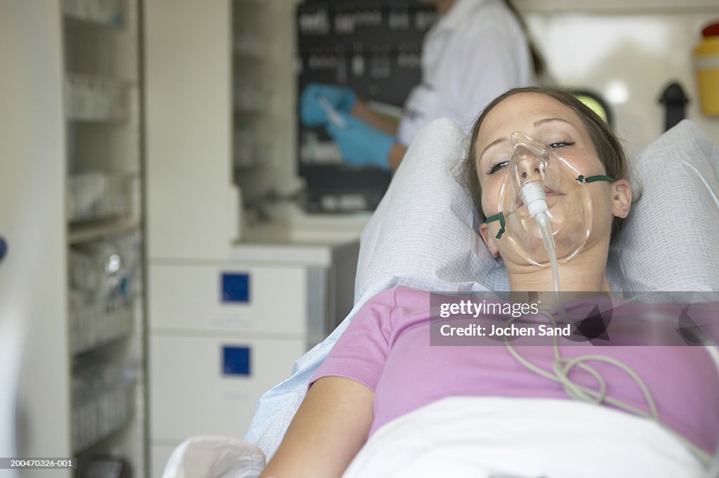 "Female patient in ambulance, wearing oxygen mask, eyes open"
