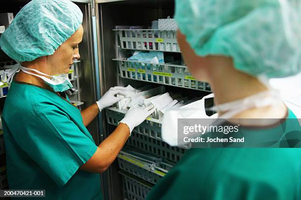operating theatre staff wearing scrubs, one looking through supplies - medische artikelen stockfoto's en -beelden