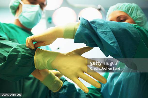 "operating theatre staff wearing scrubs,one helping other put on gloves" - surgical glove stock pictures, royalty-free photos & images