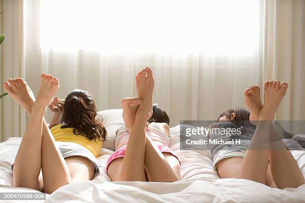 three young women lying side by side on bed, rear view - woman lying on stomach with feet up stock pictures, royalty-free photos & images
