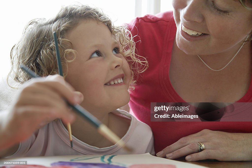 "Girl (3-5) painting picture, looking up at mother, smiling"