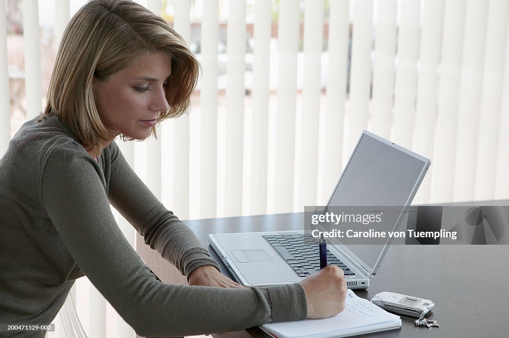 Teenage girl (14-16) with laptop writing on pad