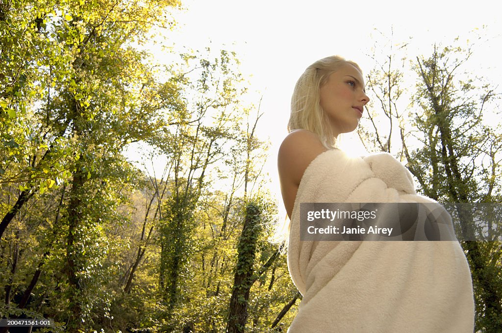 Young woman in woods, wrapped in towel, low angle view