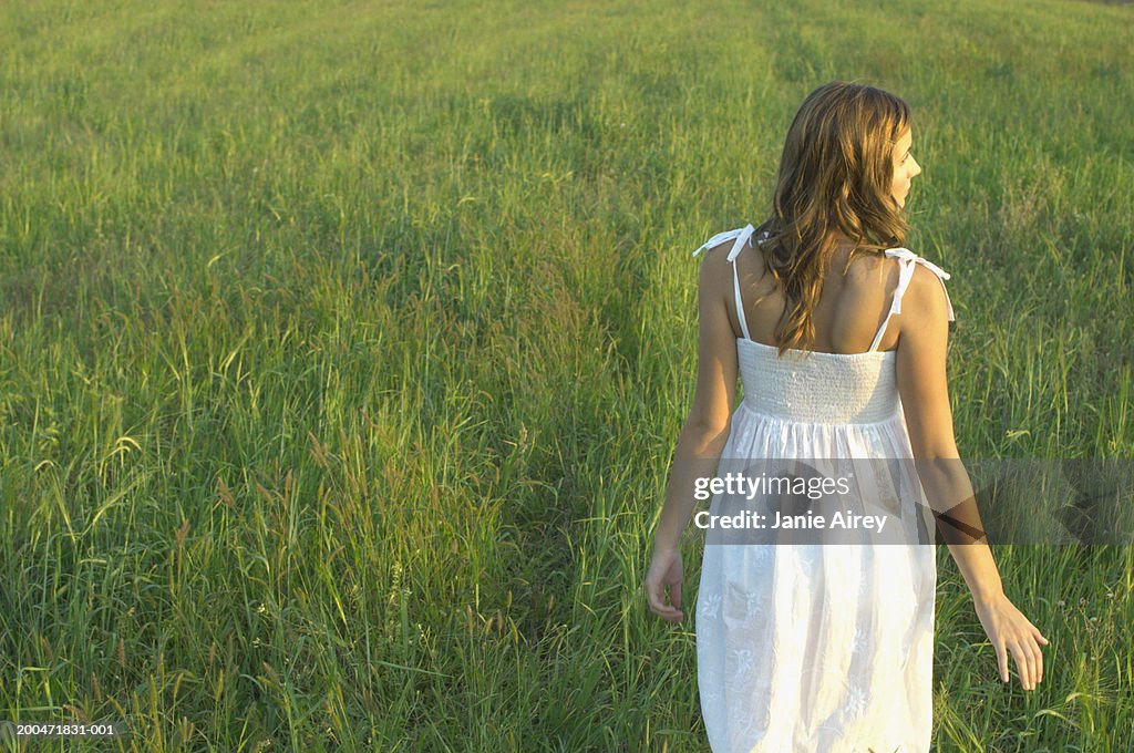 Teenage girl (16-18) walking through long grass, rear view