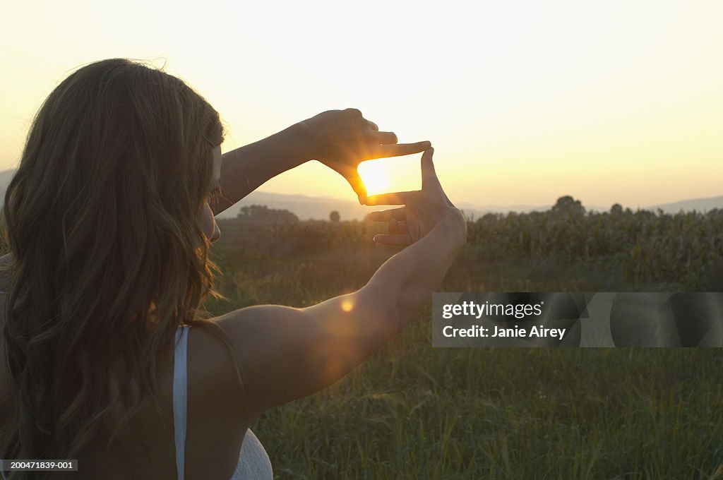 Teenage girl (16-18) outdoors, "framing" sun with fingers