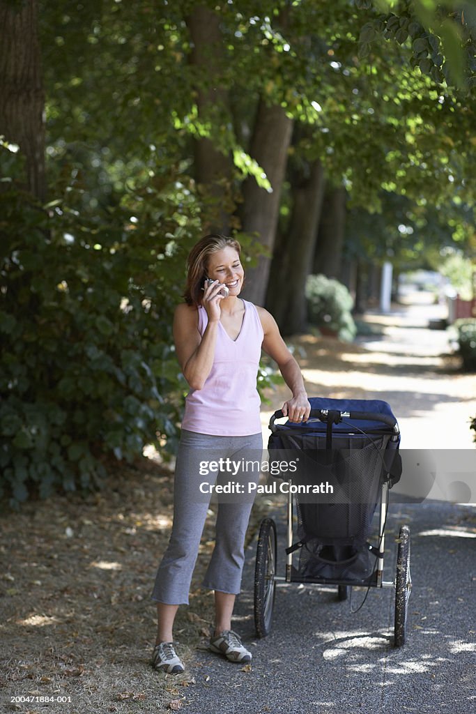Young woman with baby stroller talking on cell phone, smiling