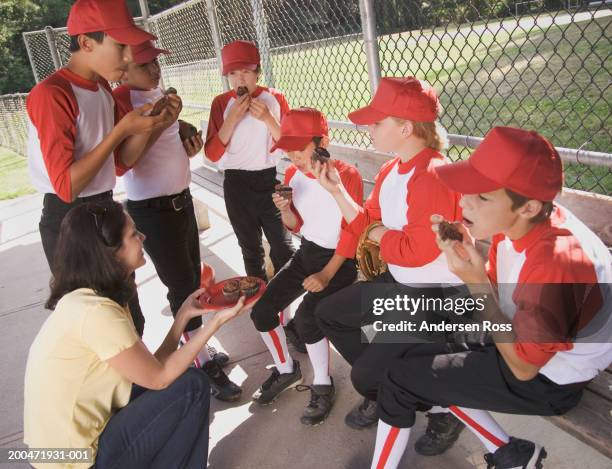 mother giving cupcakes to boys (9-12) in baseball dugout - baseball mom stock pictures, royalty-free photos & images