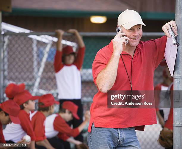 coach on cell phone, boys (9-11) in baseball dugout in background - kids call 911 stock pictures, royalty-free photos & images