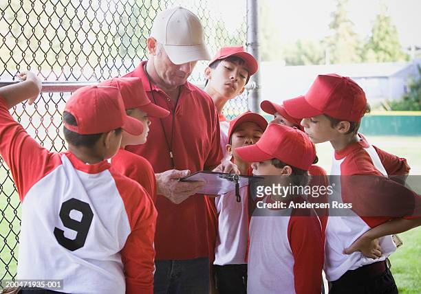 coach and baseball players (9-11) looking at clipboard in dugout - sports dugout fotografías e imágenes de stock