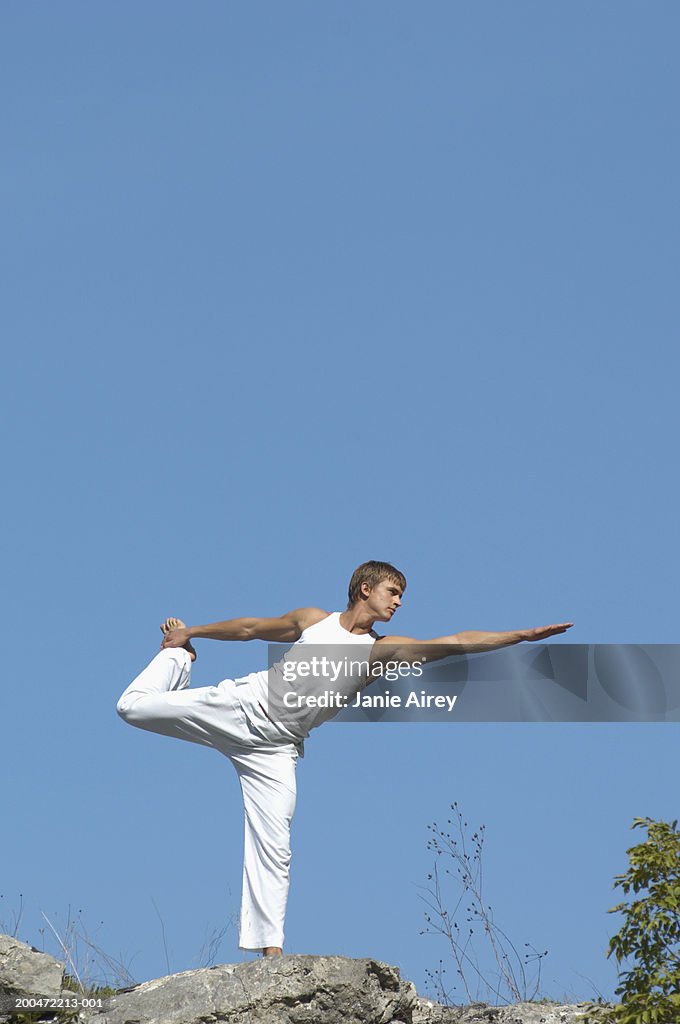 Young man practicing yoga on rock in mountain landscape,low angle view