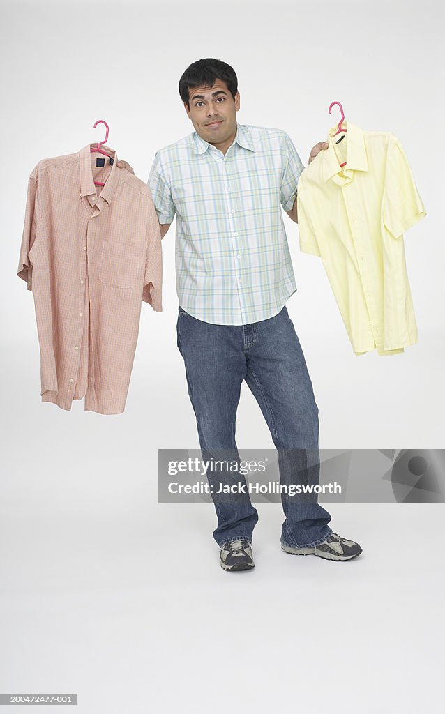 Portrait of a mid adult man holding two shirts on hangers