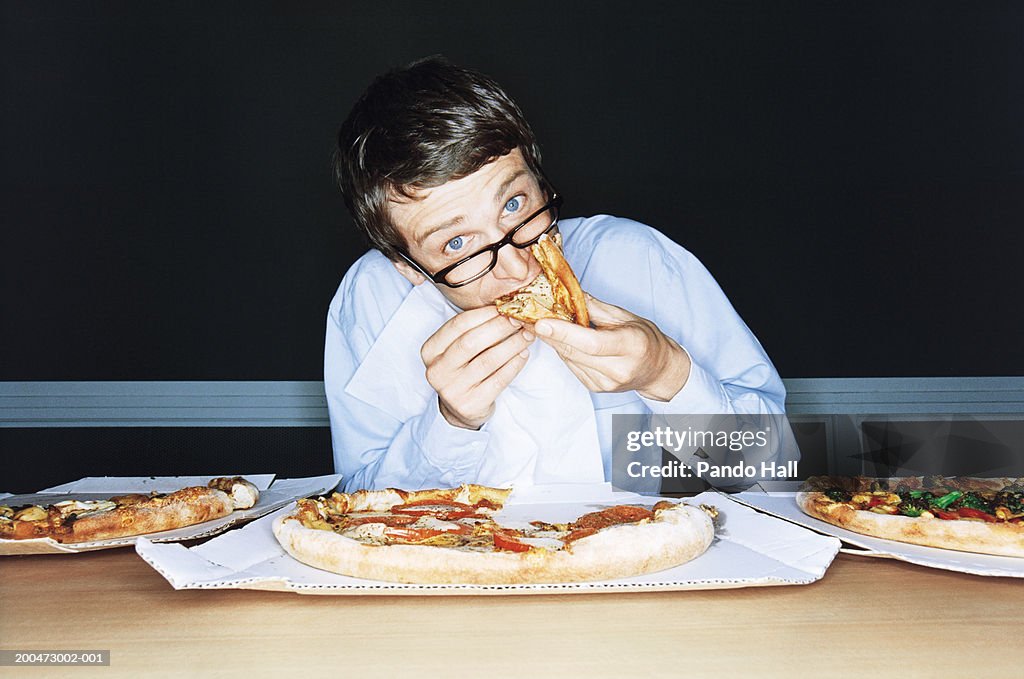 Businessman eating pizza from boxes on table, portrait