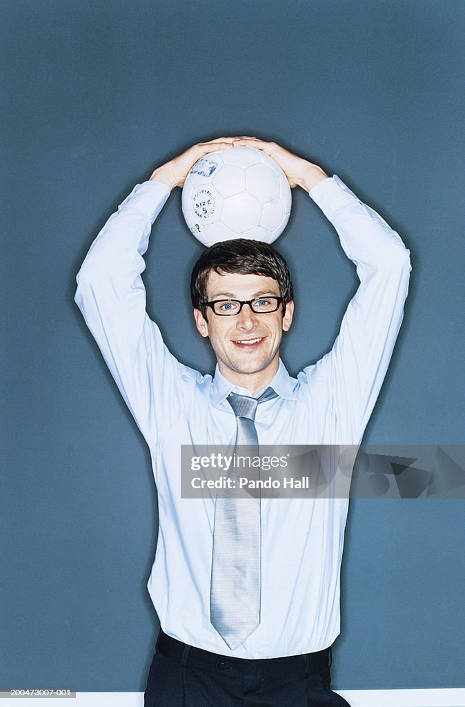 Businessman holding football over head, smiling, portrait