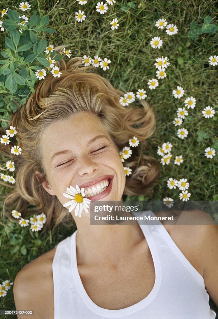 Young woman lying on grass, with daisy in mouth, smiling