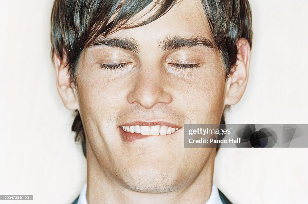 Young man biting lip, smiling, eyes closed, close-up