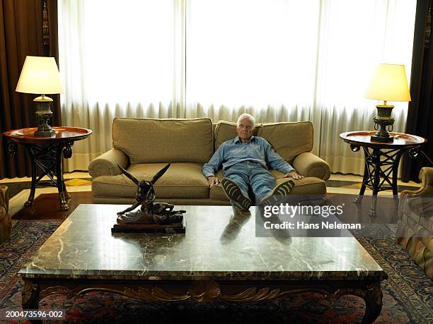 senior man relaxing on sofa, propping feet on table - fatigue full body stock pictures, royalty-free photos & images