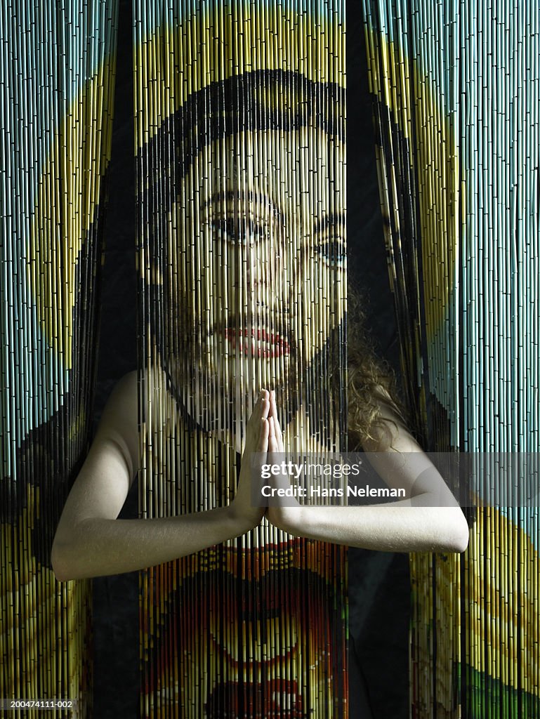 Young woman putting hands through beaded curtain with image of Jesus